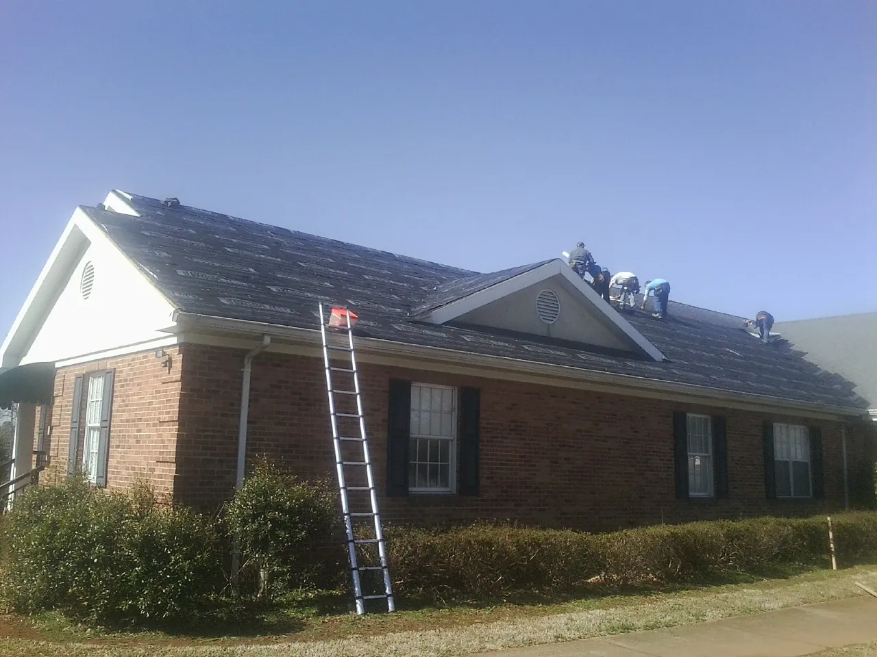 Crew tearing shingles off a brick ranch roof with a ladder set — Emergency Roof Repair work by our crew in Elmwood
