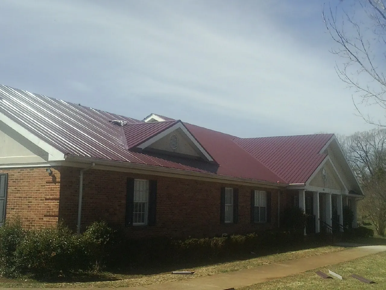 Red metal roof with gabled entries on a long brick building, from a Hail Damage Roof Repair job in Elmwood