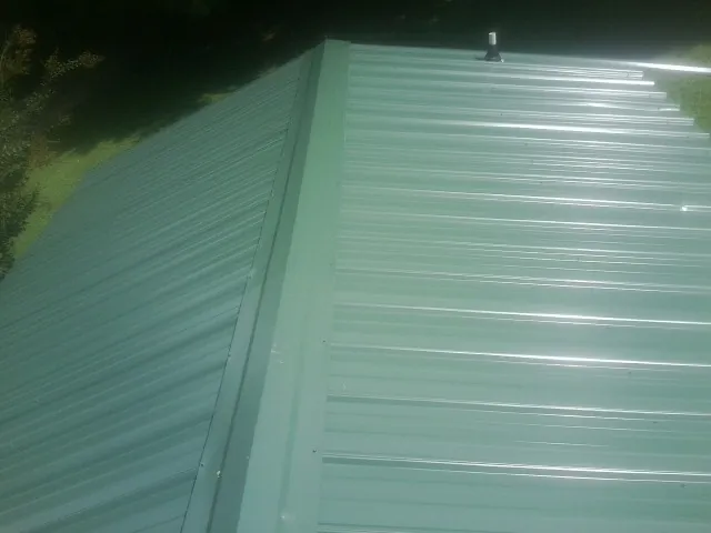 New green metal panels meeting at the ridge of a roof — Flat Roof Repair work by our crew in Elmwood